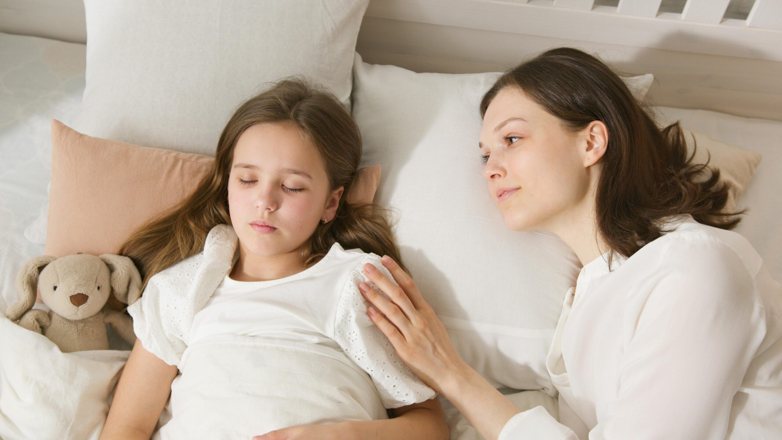 A loving mother gently watches her daughter sleep peacefully in bed.