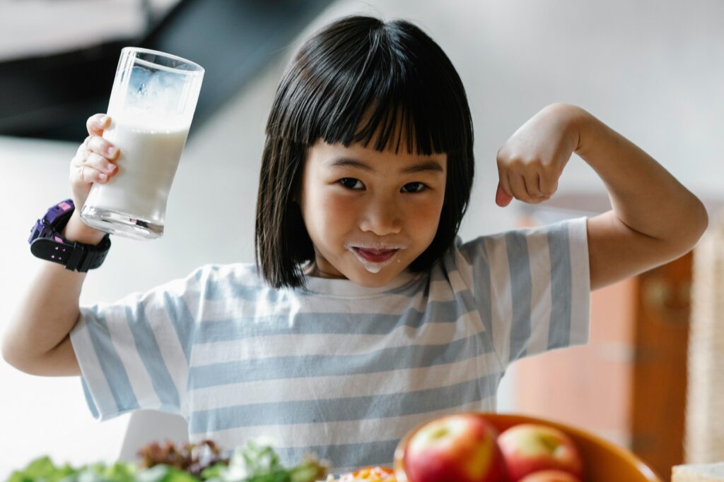 A happy child drinking milk and flexing muscles, promoting a healthy breakfast habit.