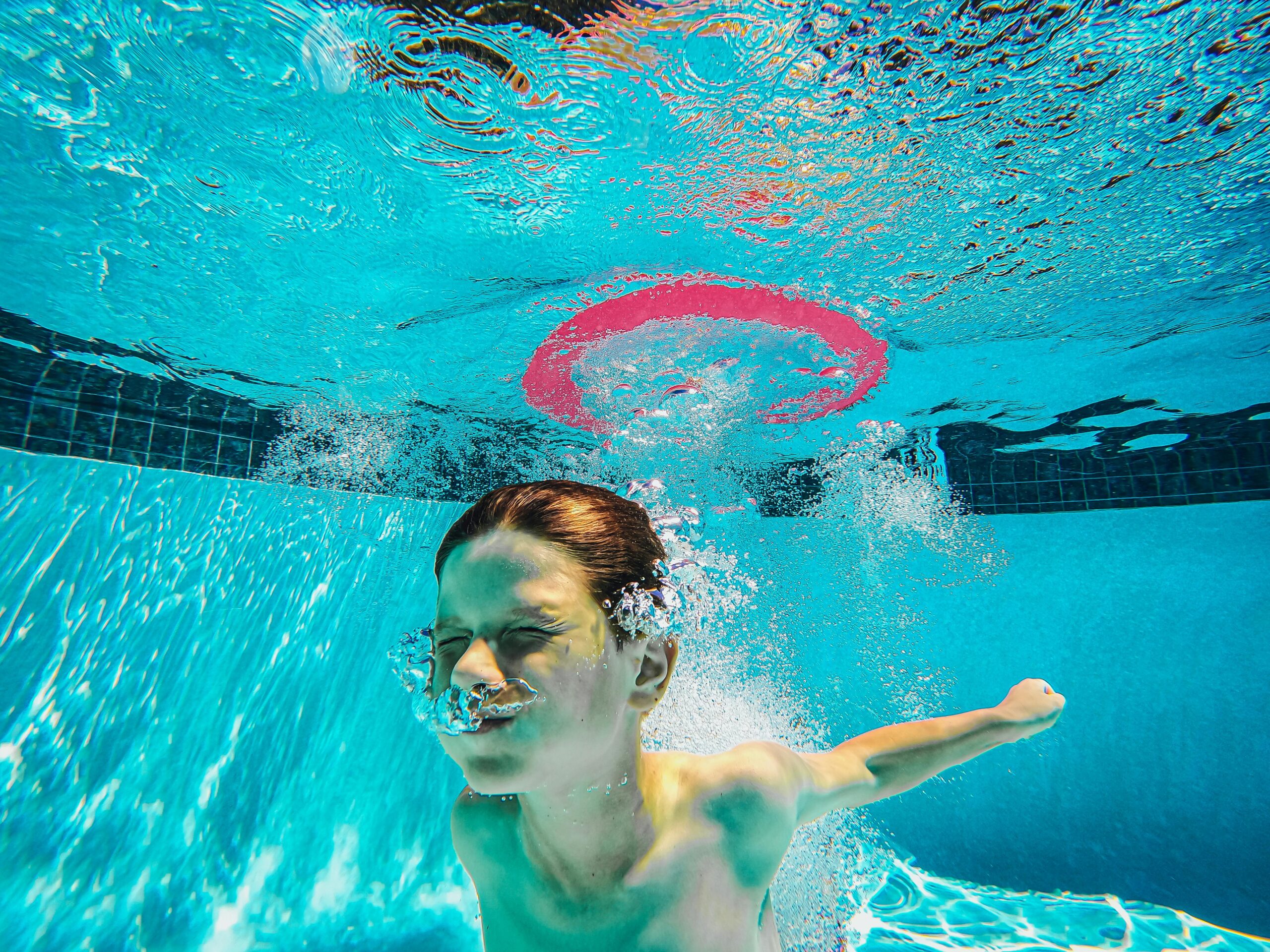 A child energetically plays underwater in a swimming pool, surrounded by bubbles and splashes.