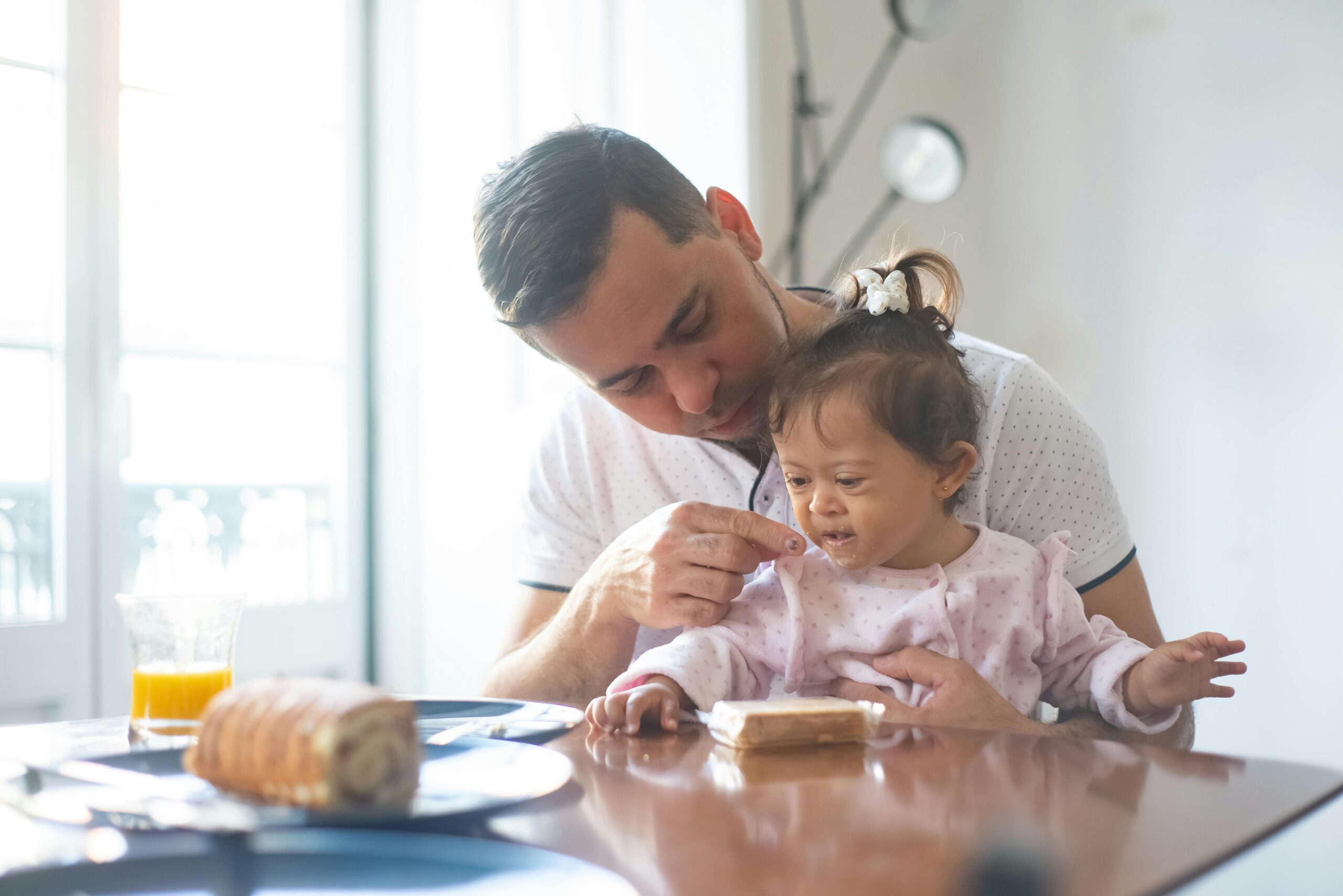 Father lovingly feeds daughter with Down syndrome during breakfast at home.