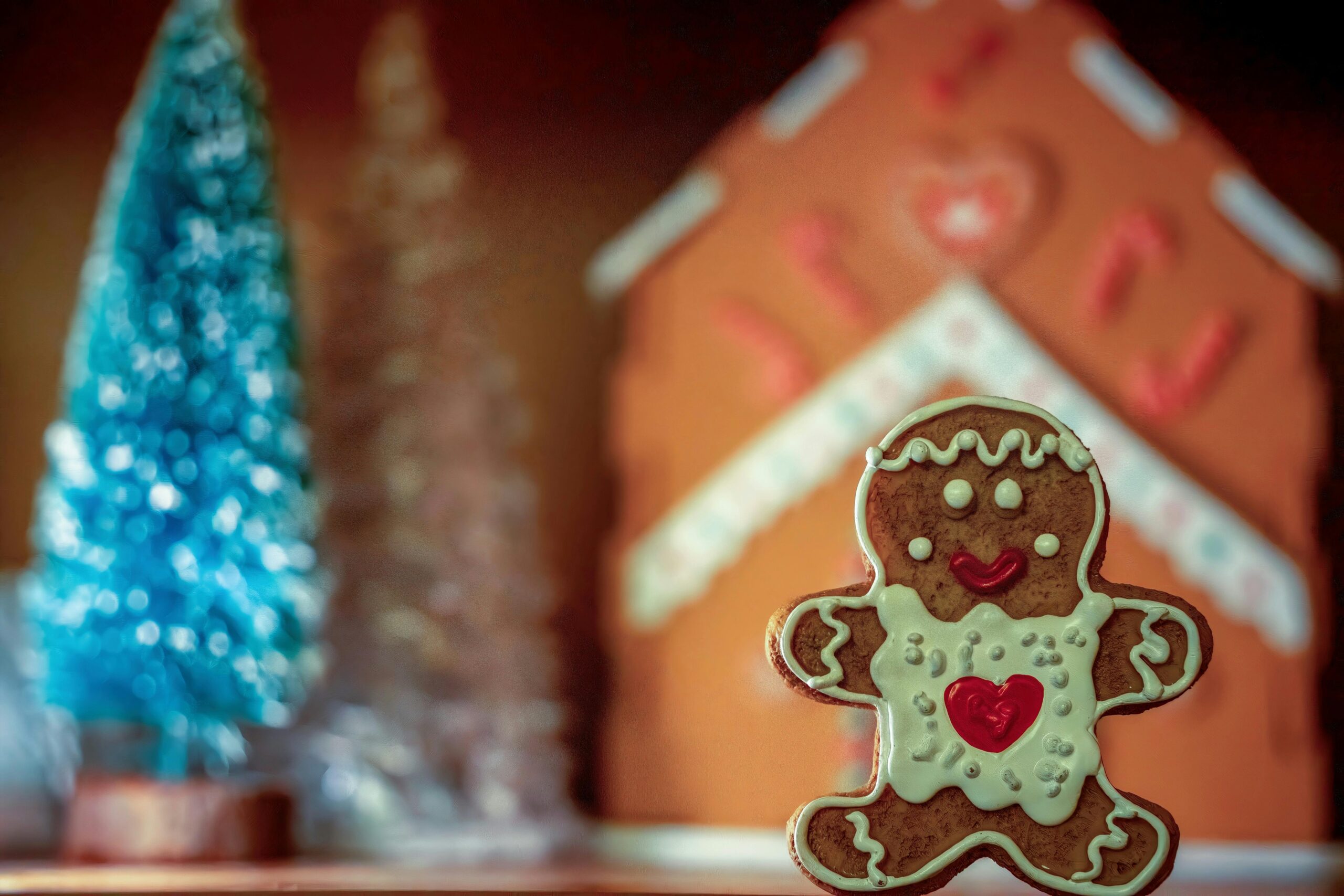Charming gingerbread man cookie with icing, set in a festive holiday scene with gingerbread house backdrop.