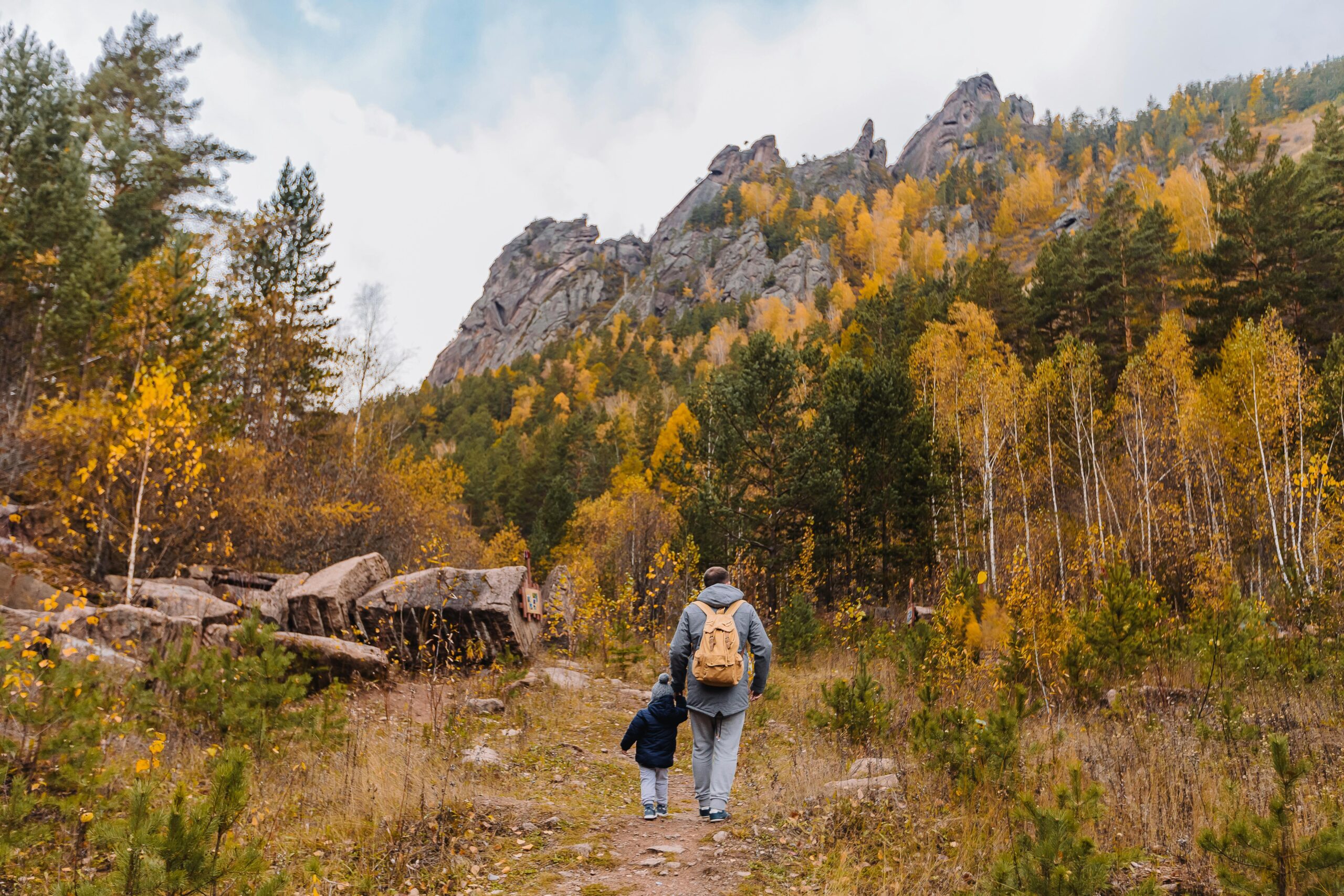 A father and son hiking together in an autumn mountain forest, surrounded by colorful trees.