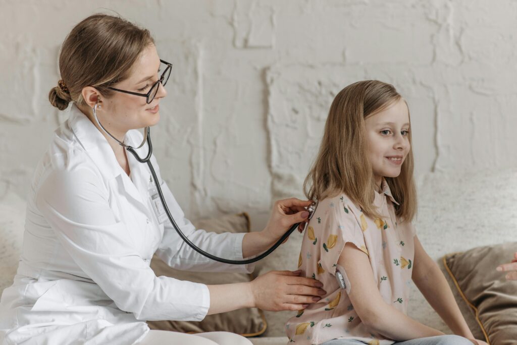 A doctor uses a stethoscope during a check-up with a young girl in a medical setting.
